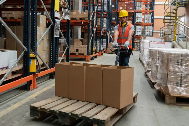 Worker moving pallets with a pallet jack in a warehouse